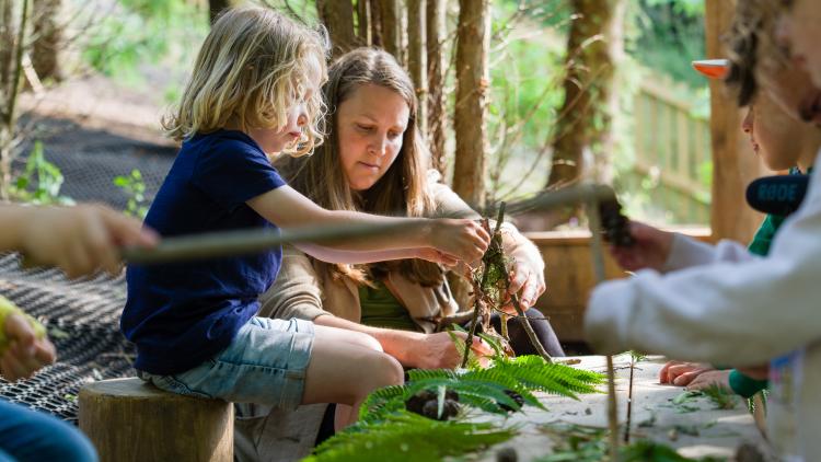 Mother and child building sculpture out of sticks and leaves sat in the woods