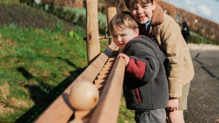 Two children throwing wooden marble down marble run
