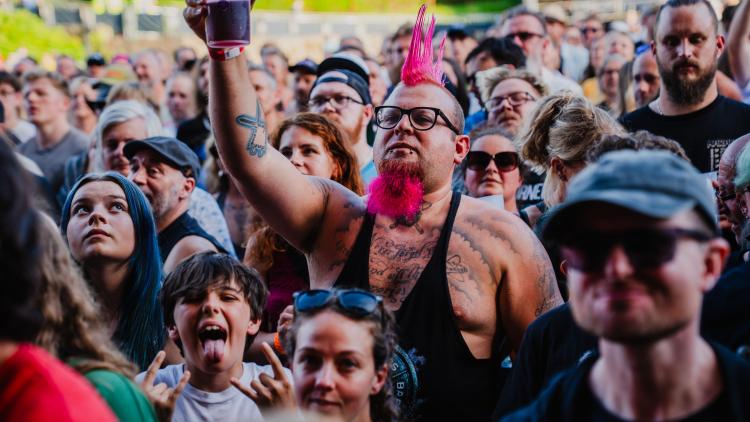 Man with pink mohawk raising cup in gig crowd