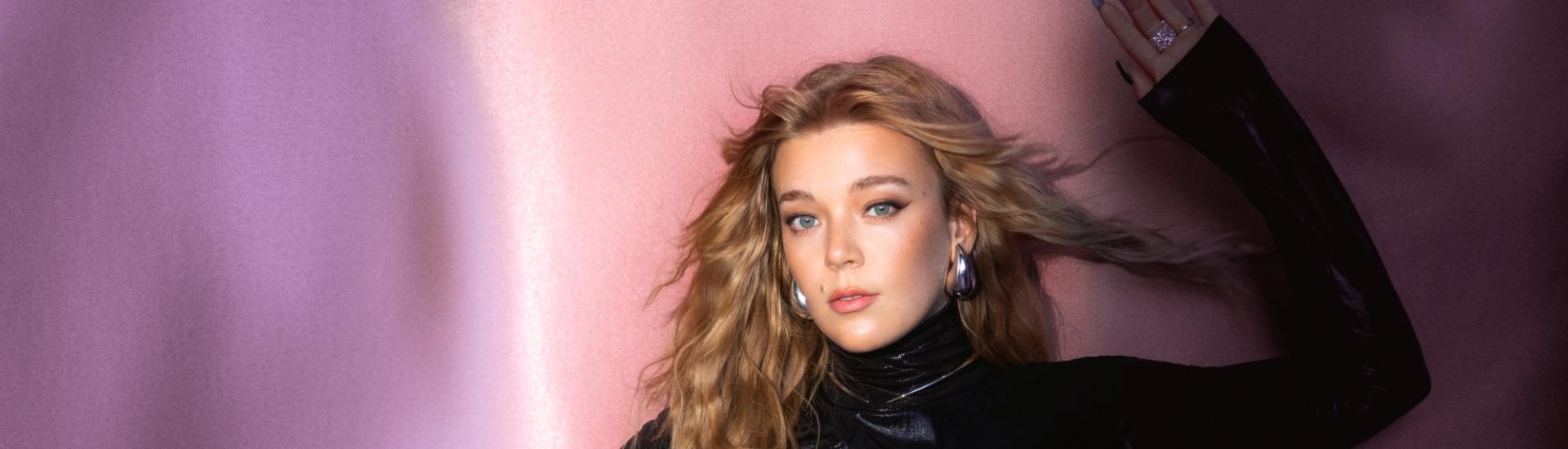 Becky Hill stood in front of coloured drape