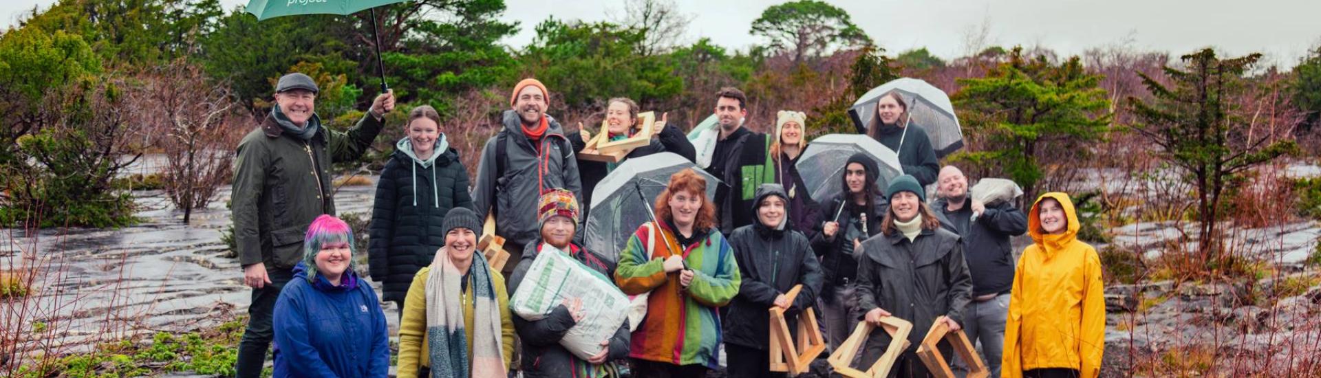 A group of people standing in a mossy stony landscape. The weather is grey but they are dressed colourfully.