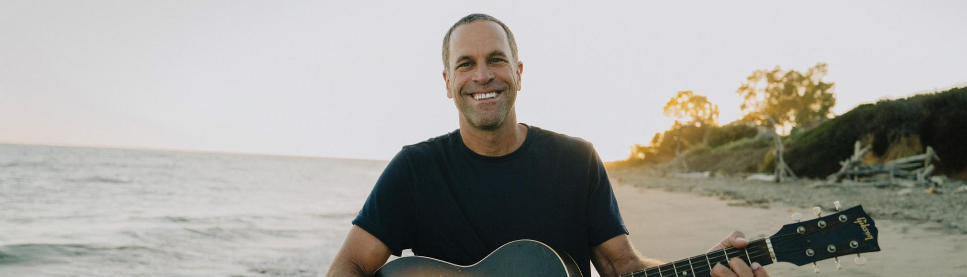 Jack Johnson on a beach holding a guitar